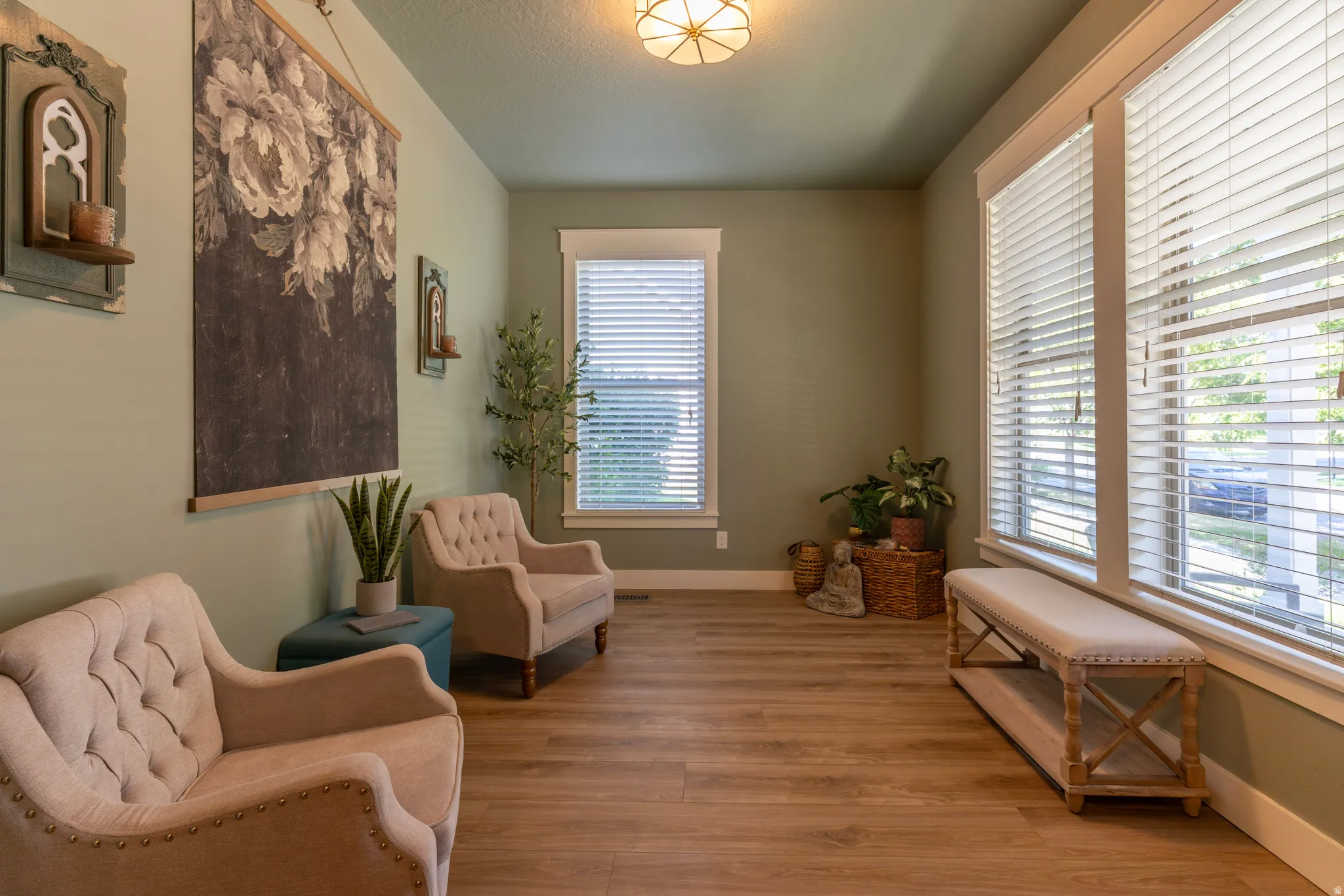 Spacious room featuring wood-finish flooring, multiple windows with blinds, a prominent ceiling light fixture, and light green painted walls