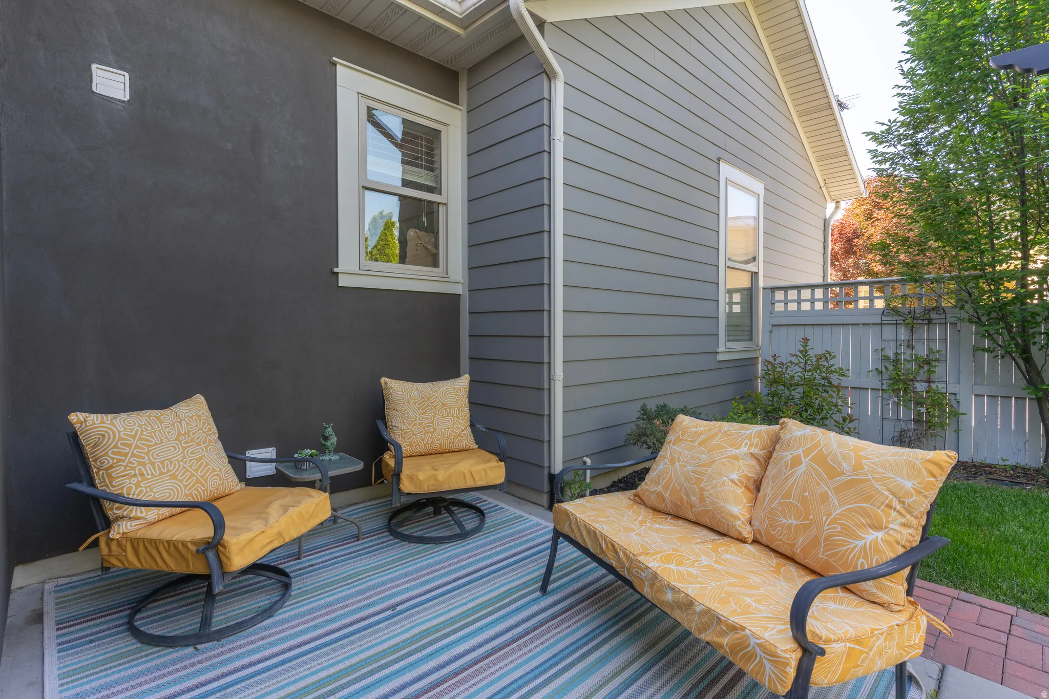 Private patio area featuring a striped outdoor rug, dark stucco exterior wall, and horizontal siding