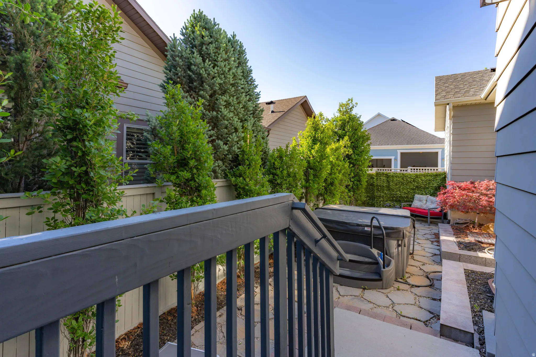 Private outdoor space featuring a hot tub, stone paver patio, raised garden beds, and mature landscaping
