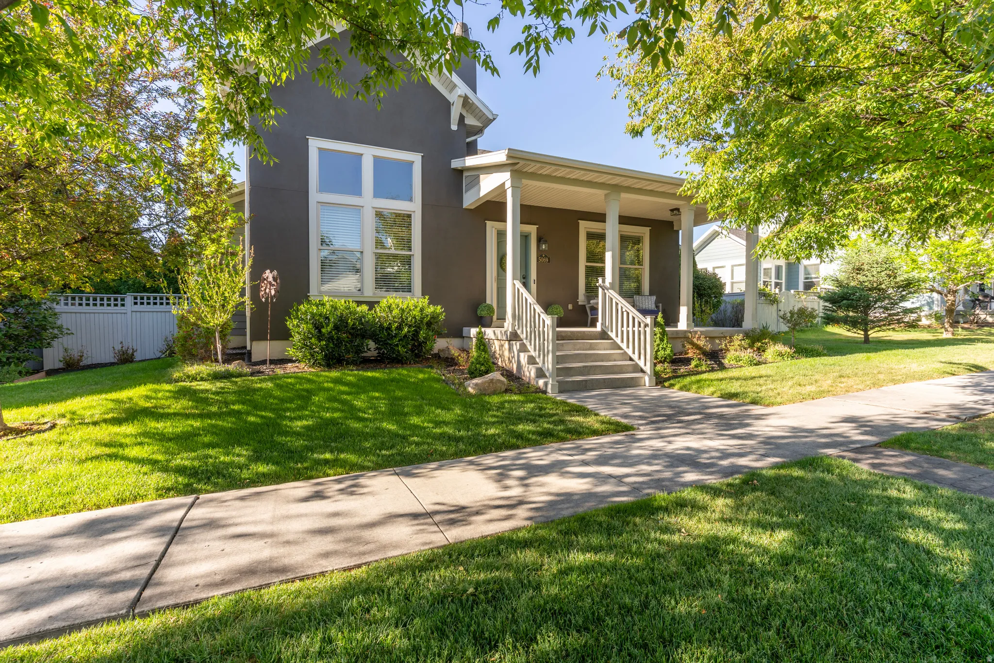 Contemporary facade with a covered front porch, white railings, and a concrete pathway