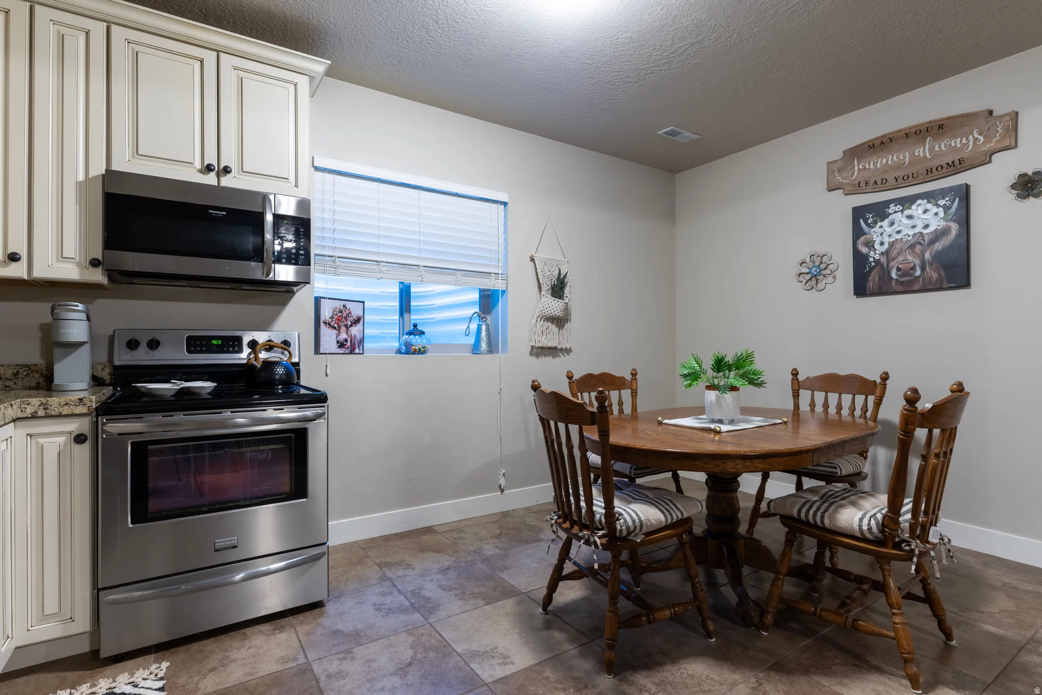 Kitchen area featuring white cabinetry, stainless steel appliances including a built-in microwave and range, light-toned countertops, and tile flooring