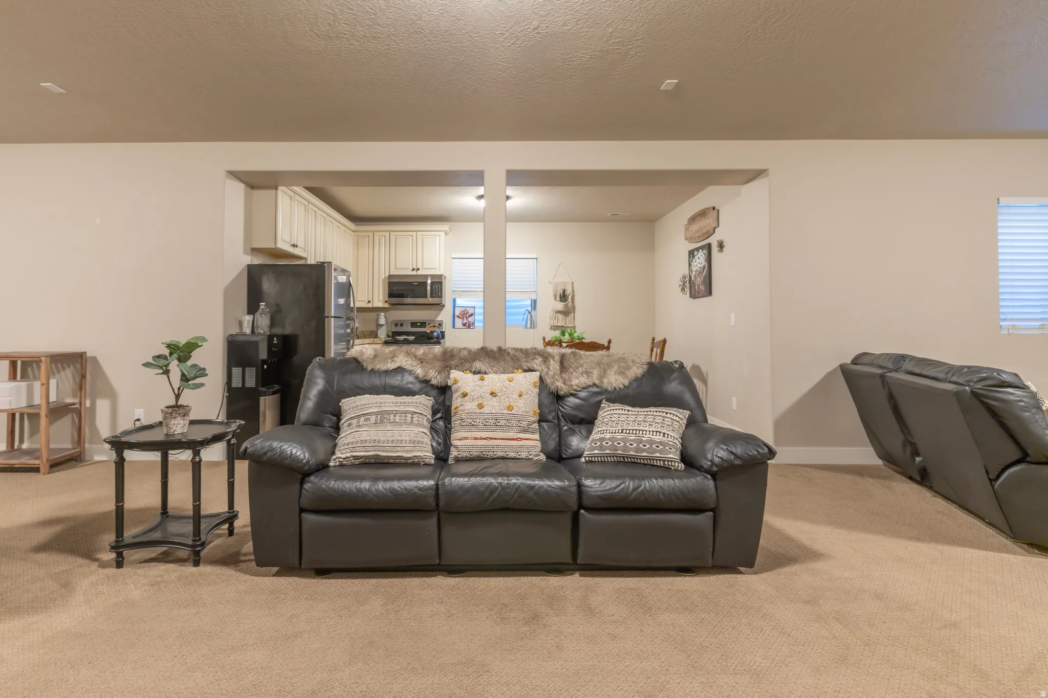 Expansive carpeted living area featuring an open archway to a kitchen with white cabinetry and stainless steel appliances