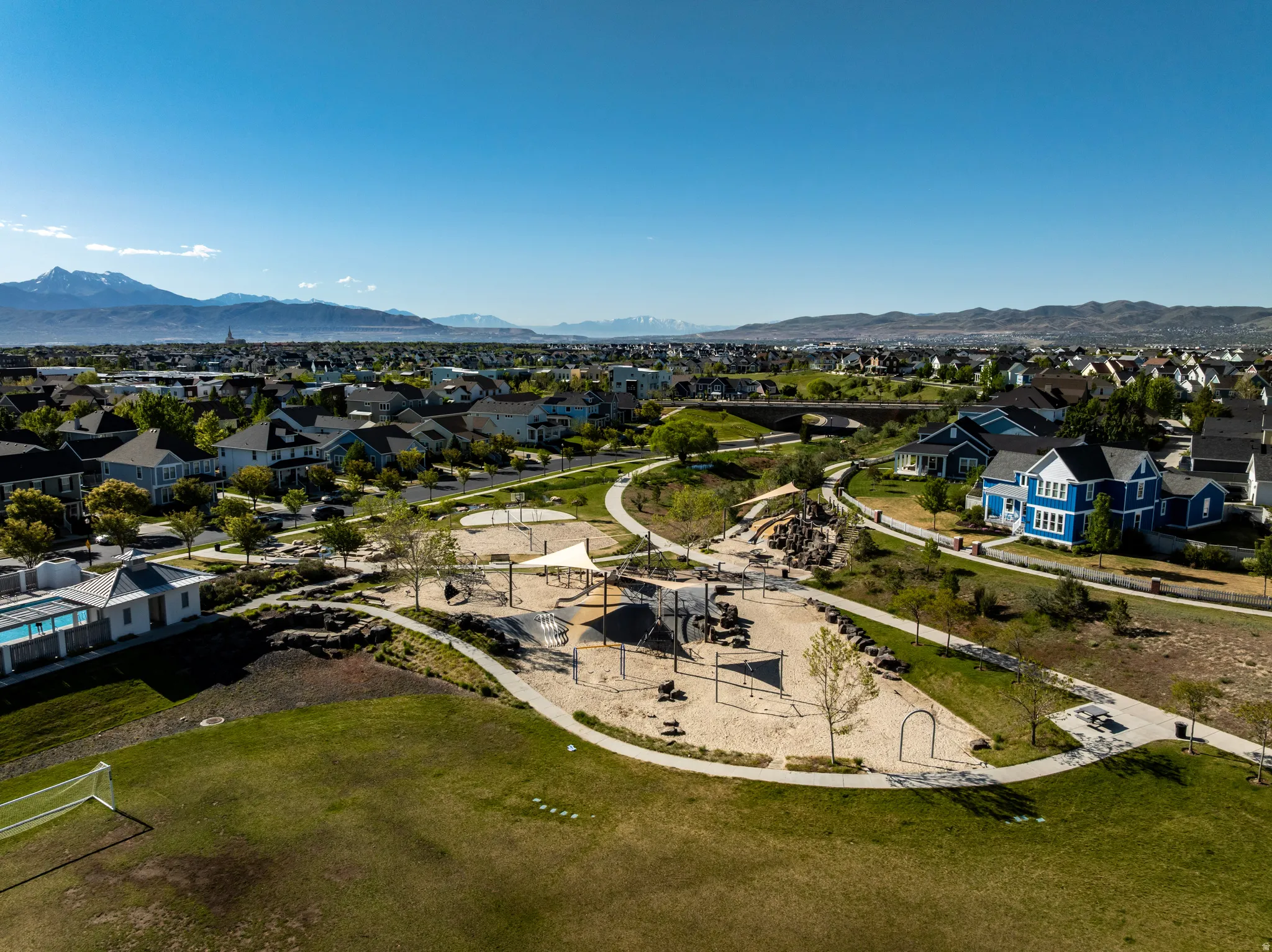 Expansive neighborhood playground with sand base and shaded structures, bordered by walking paths