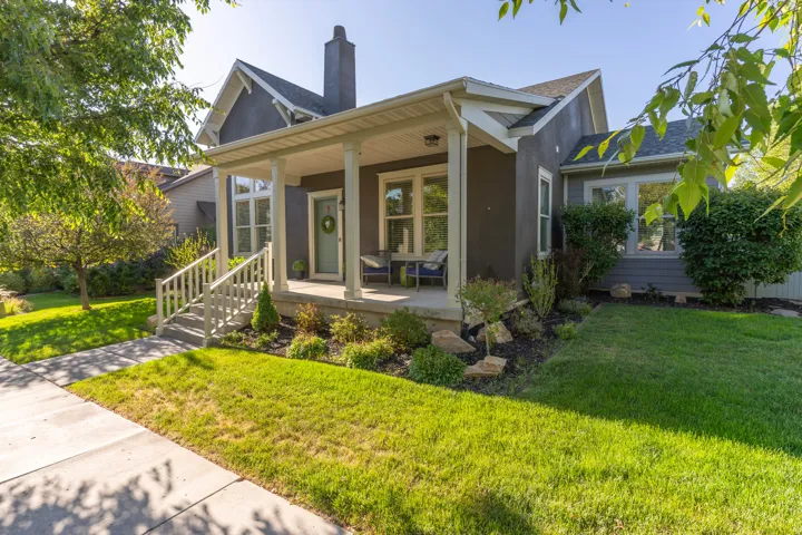 Inviting stucco exterior featuring a covered front porch with white columns, a pitched roof, a prominent chimney, and a landscaped front yard with a sidewalk