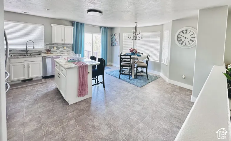 Open-concept kitchen and dining area featuring white cabinetry, a central island with countertop seating, stainless steel appliances, and tile flooring