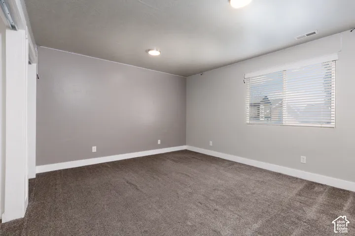 Spacious room featuring neutral grey walls and dark grey carpet.