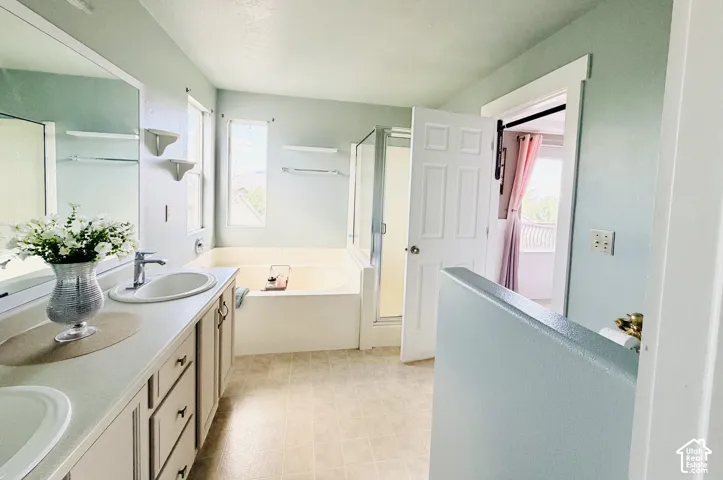Bathroom featuring a double vanity with built-in cabinetry, an integrated soaking tub, a stand-alone shower with a glass enclosure, and light-toned flooring
