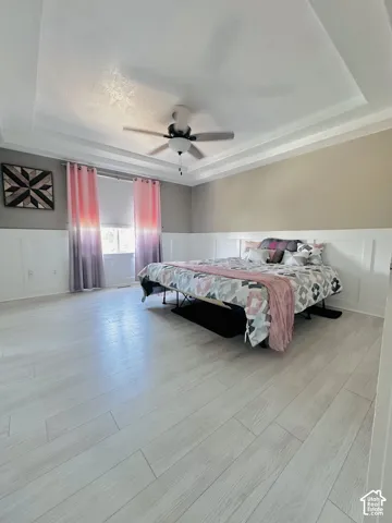 Spacious room featuring light wood-finish flooring, wainscoting, and a tray ceiling with a mounted ceiling fan