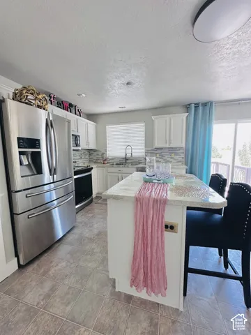 Kitchen featuring a central island with seating, white cabinetry, stainless steel appliances, and tile flooring