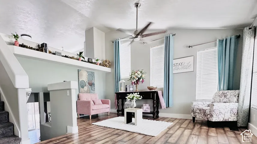 Living area featuring wood-finish flooring, two large windows with blinds, a ceiling fan, and a built-in display ledge