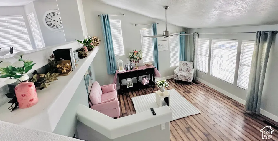 Spacious living area featuring wood-finish flooring, vaulted ceilings, and multiple windows with blinds