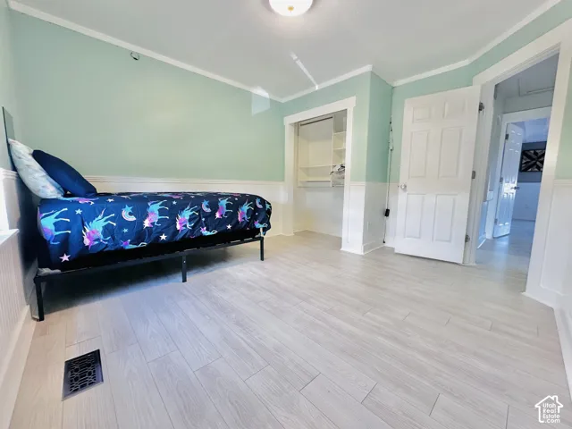 Spacious room featuring light-toned wood-finish flooring, white baseboards, and a built-in closet with shelving