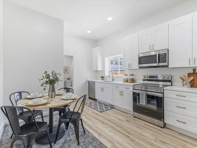 Kitchen featuring white shaker cabinetry, stainless steel appliances, light-toned countertops, and wood-finish flooring