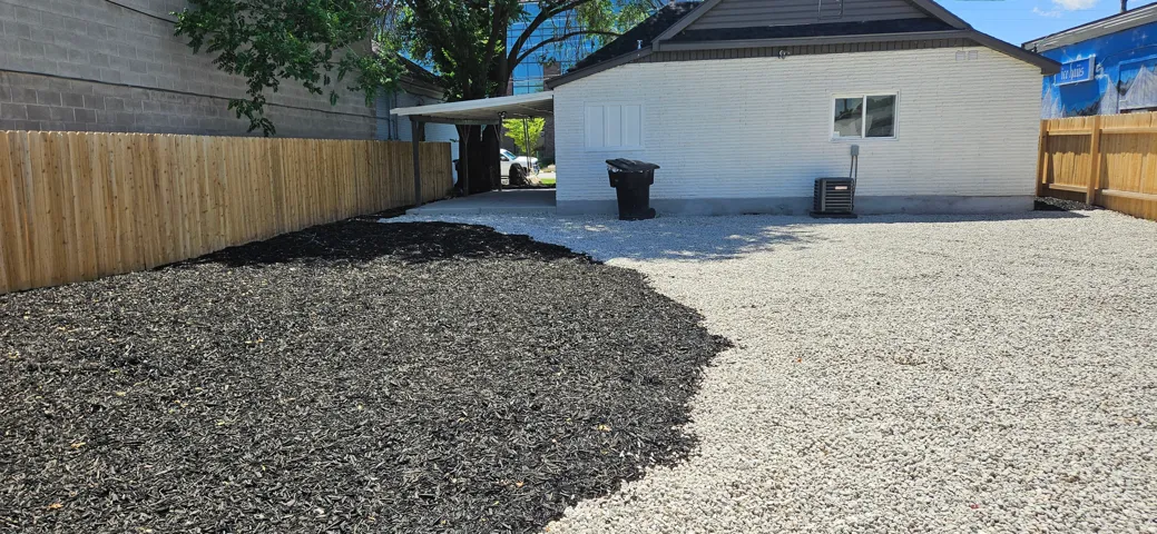 Private outdoor area featuring a new wood fence, dark mulch landscaping, and a gravel surface