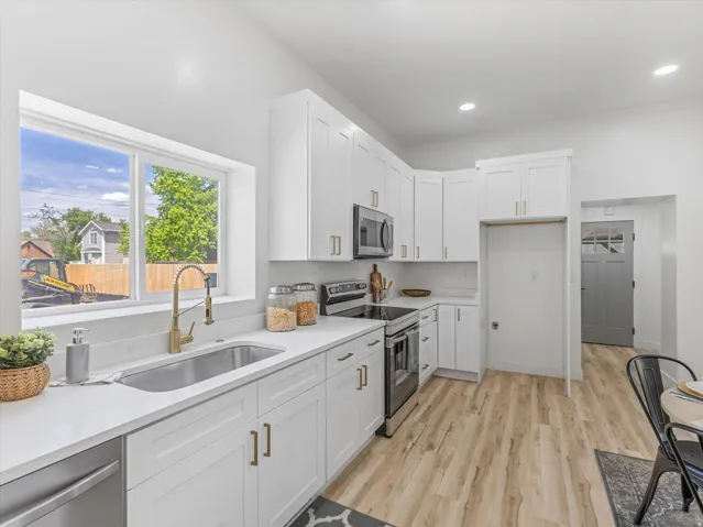 Contemporary kitchen featuring white cabinetry with gold-finish hardware, stainless steel appliances, and wood-finish flooring