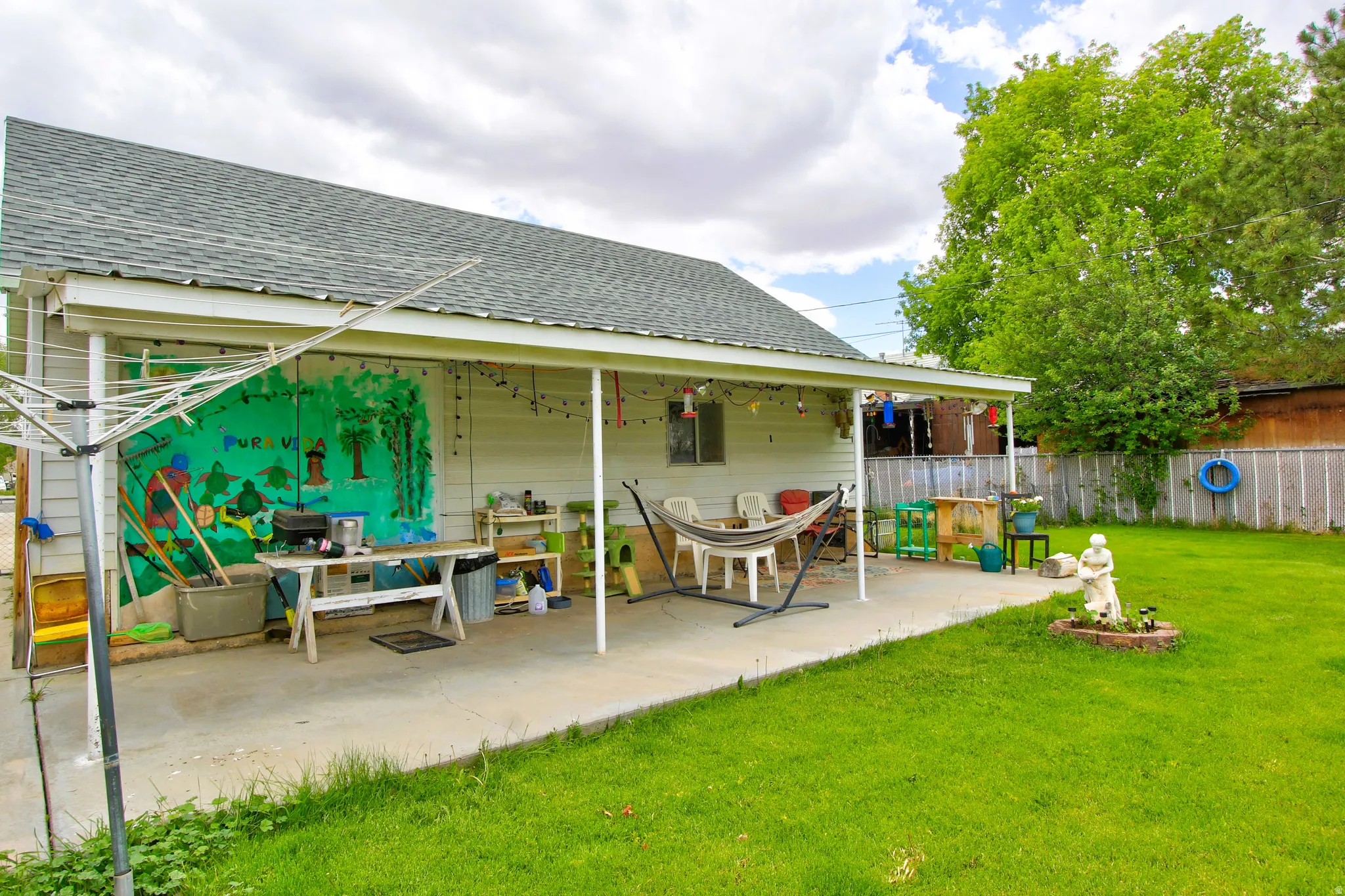 Expansive backyard featuring a concrete patio with a covered section, bordered by a vibrant green lawn