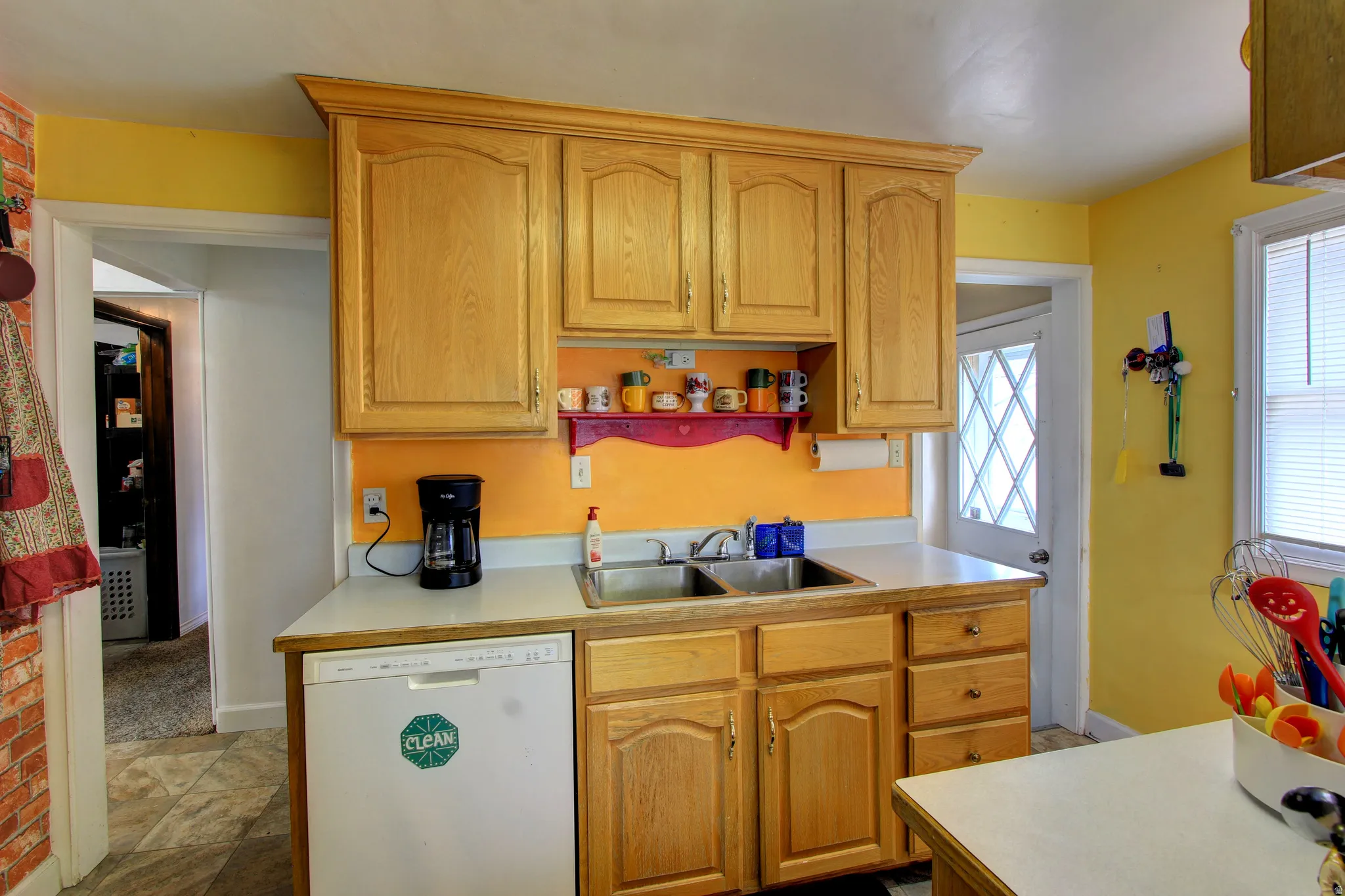 Kitchen featuring wood cabinetry with crown molding, a white laminate countertop, stainless steel double basin sink, and a built-in dishwasher