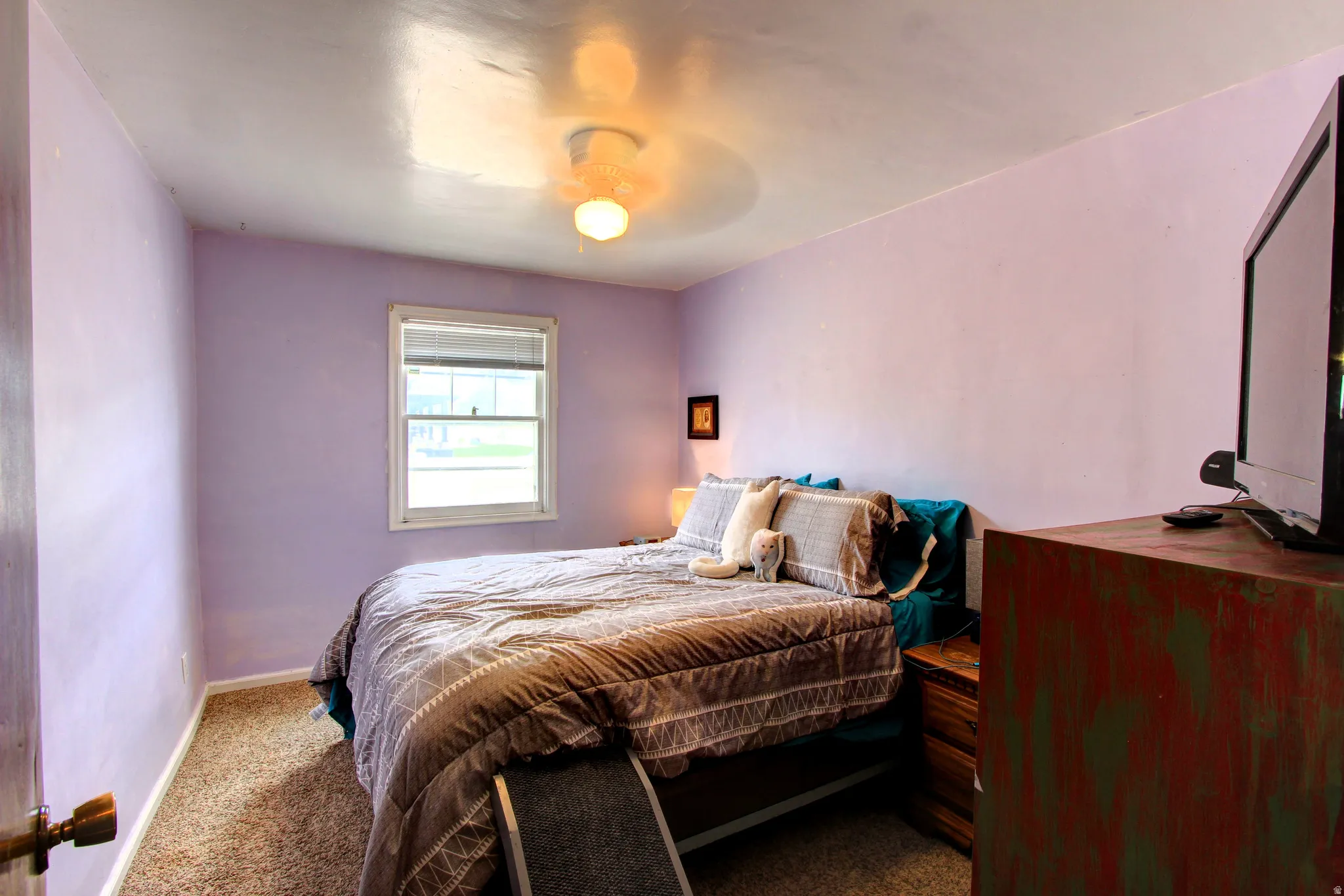 Bedroom featuring a window with blinds, light purple walls, and a ceiling fan with integrated lighting