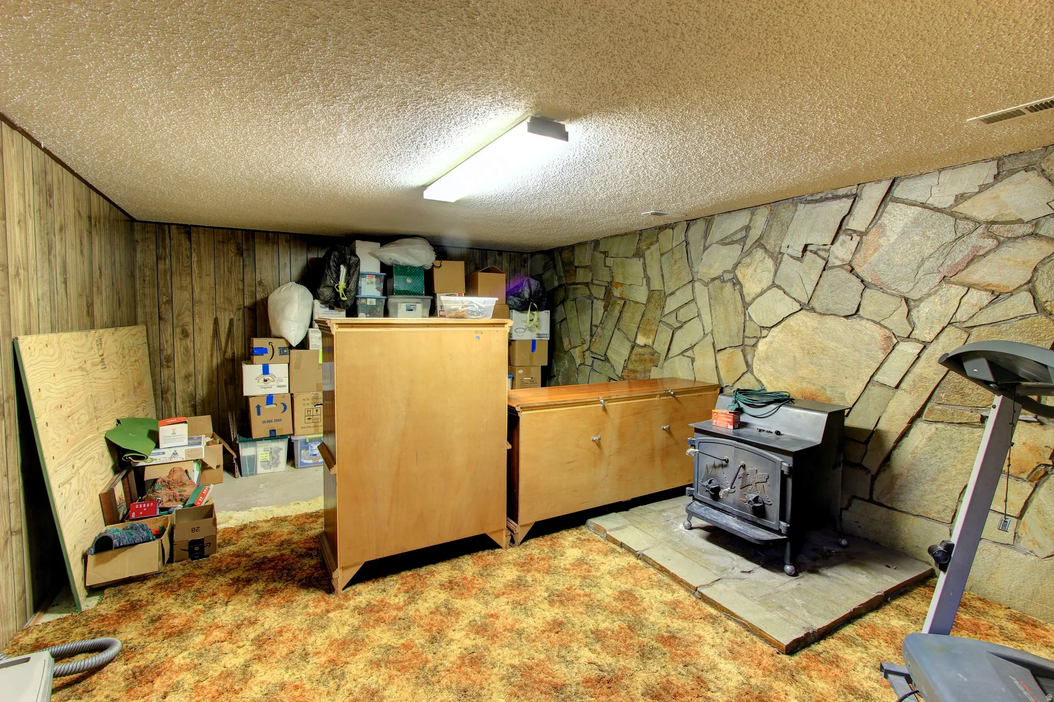 Room featuring a stone accent wall, wood paneling, and a wood-burning stove on a stone hearth