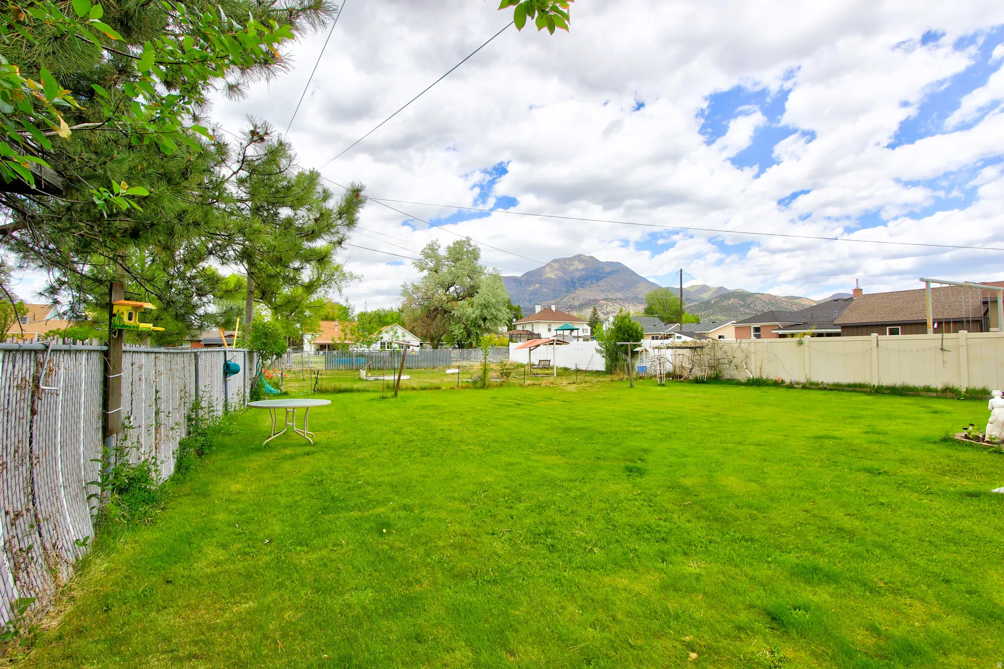 Expansive grassy backyard featuring a chain-link fence, a privacy fence, and distant mountain scenery
