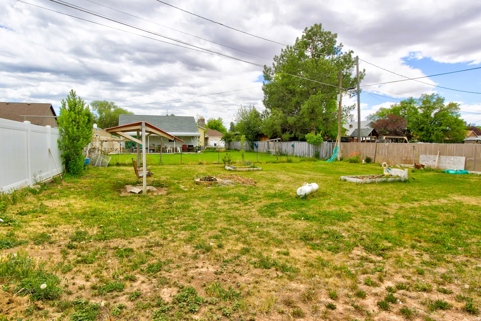 Expansive backyard featuring a white vinyl fence, established trees, and multiple raised garden beds