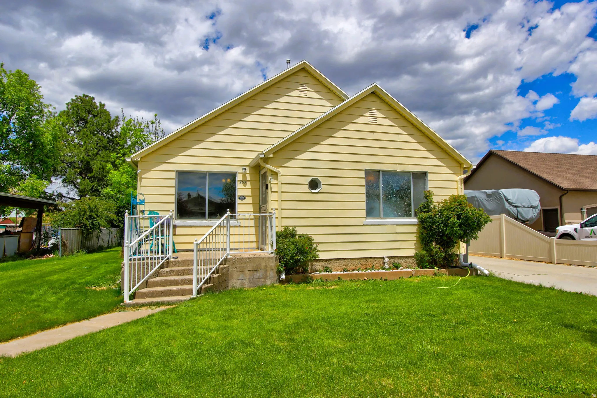 Yellow siding exterior with white trim, featuring a concrete front porch with white railings, a circular window, and a concrete pathway leading to the entrance