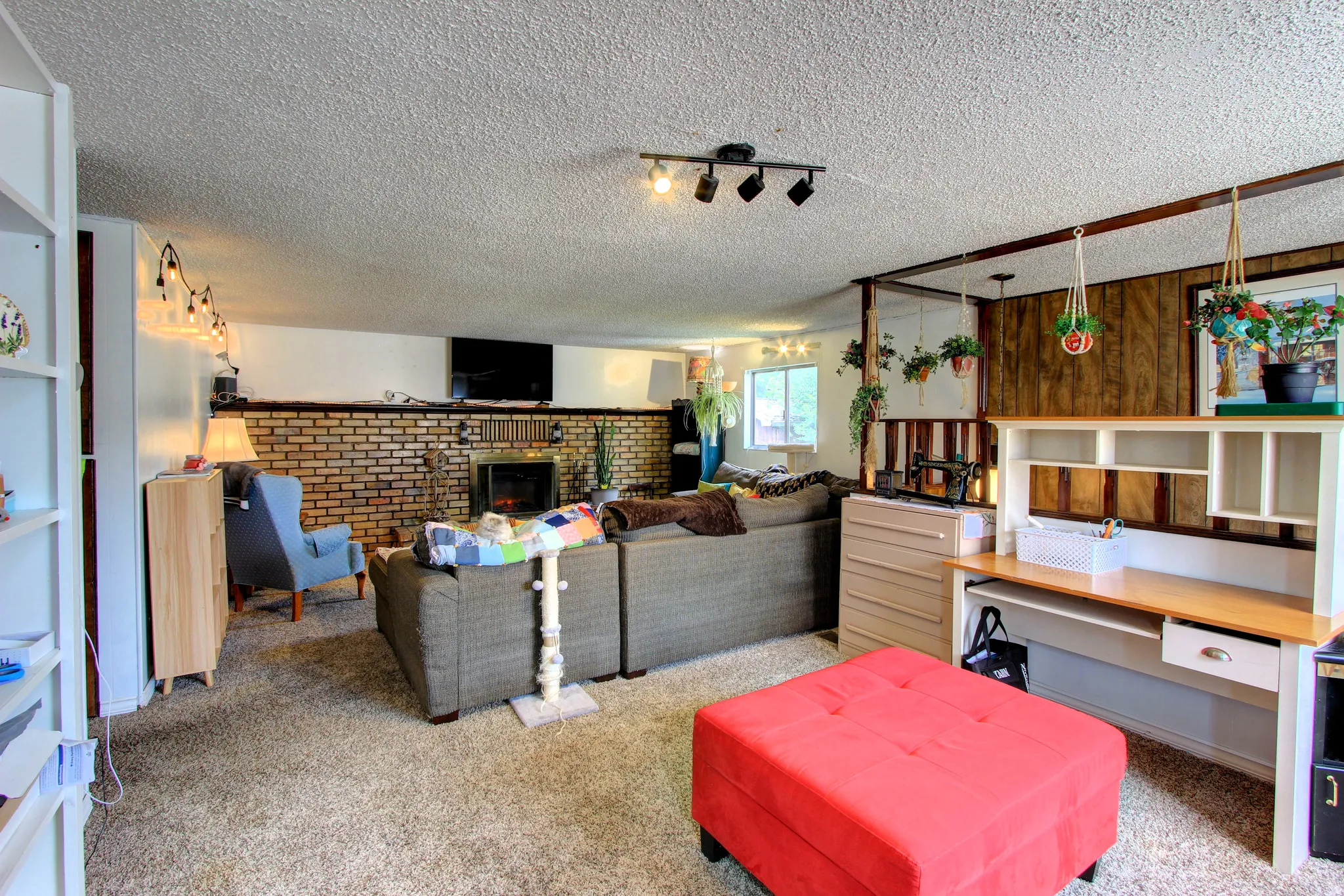 Living area featuring a brick-faced fireplace with a metal insert, track lighting, and textural carpeting
