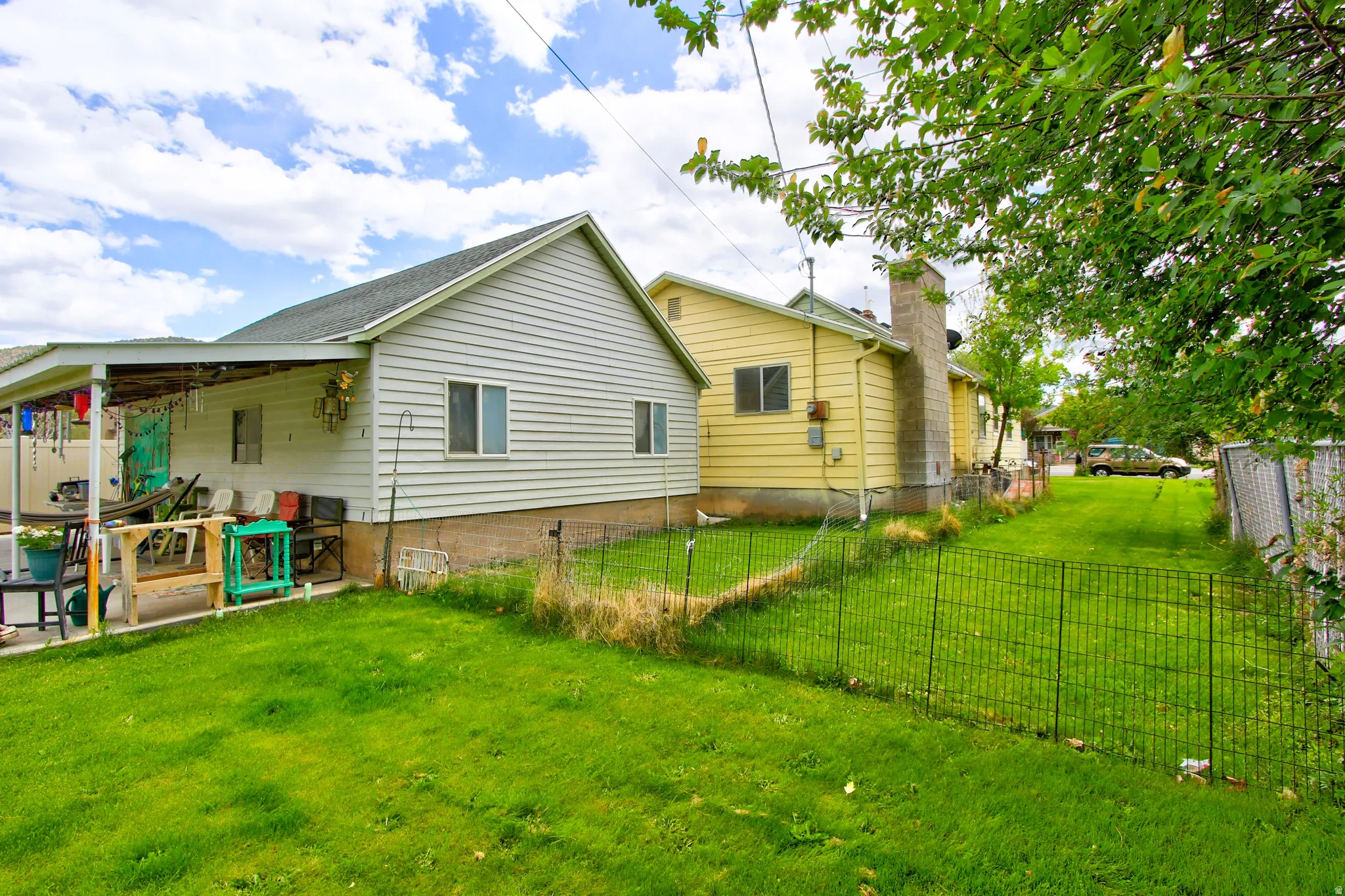 Expansive green space featuring two distinct structures with siding exteriors, a covered patio, and partial fencing