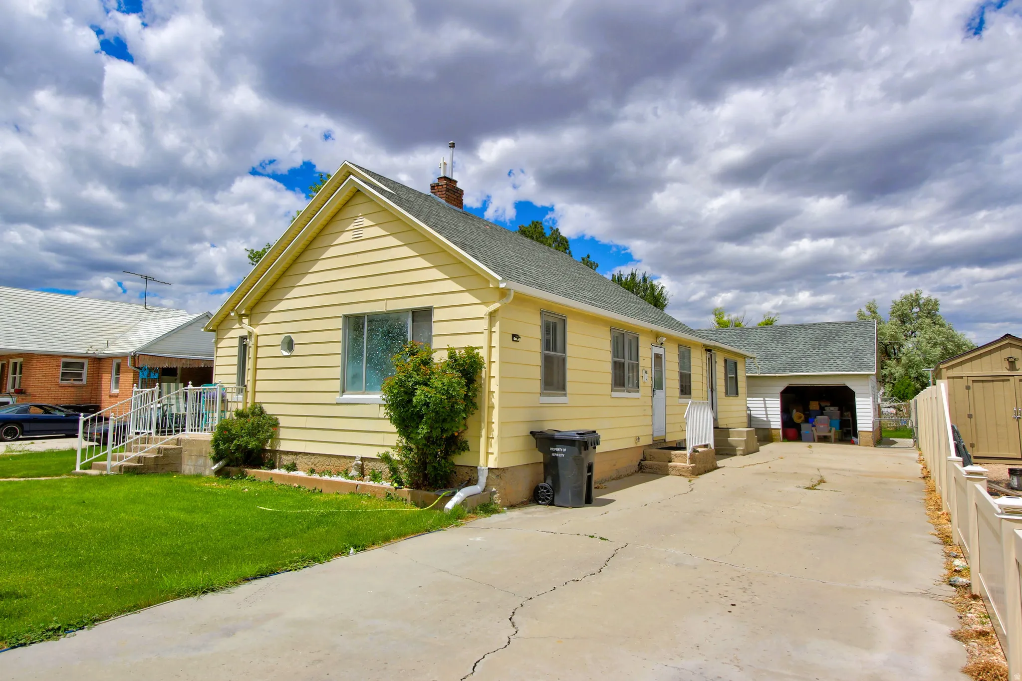 Yellow siding exterior with a pitched roof, front entry stairs with handrails, and a concrete driveway