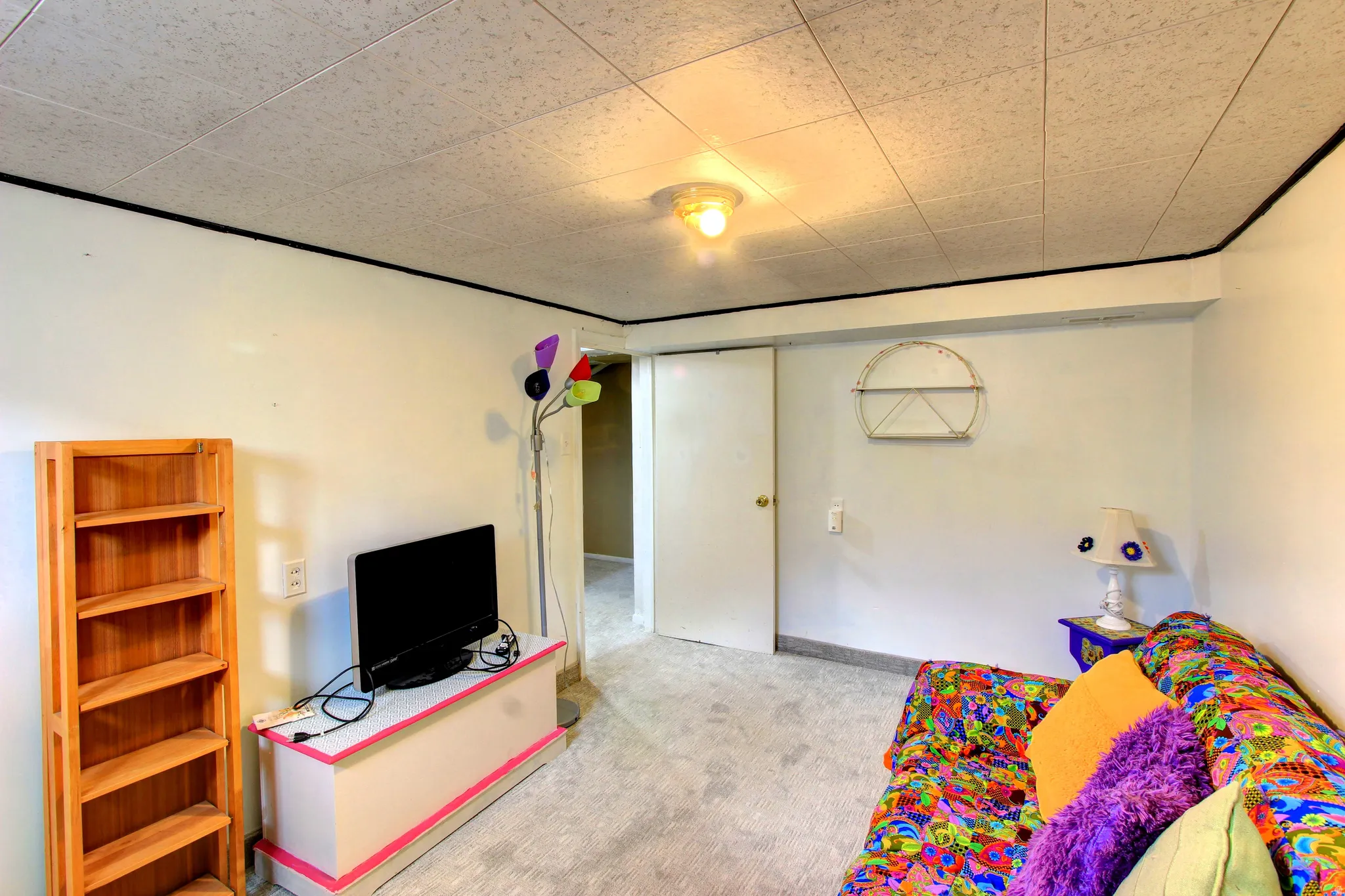 Carpeted room with a drop ceiling, featuring white walls and a white door, with a ceiling-mounted light fixture
