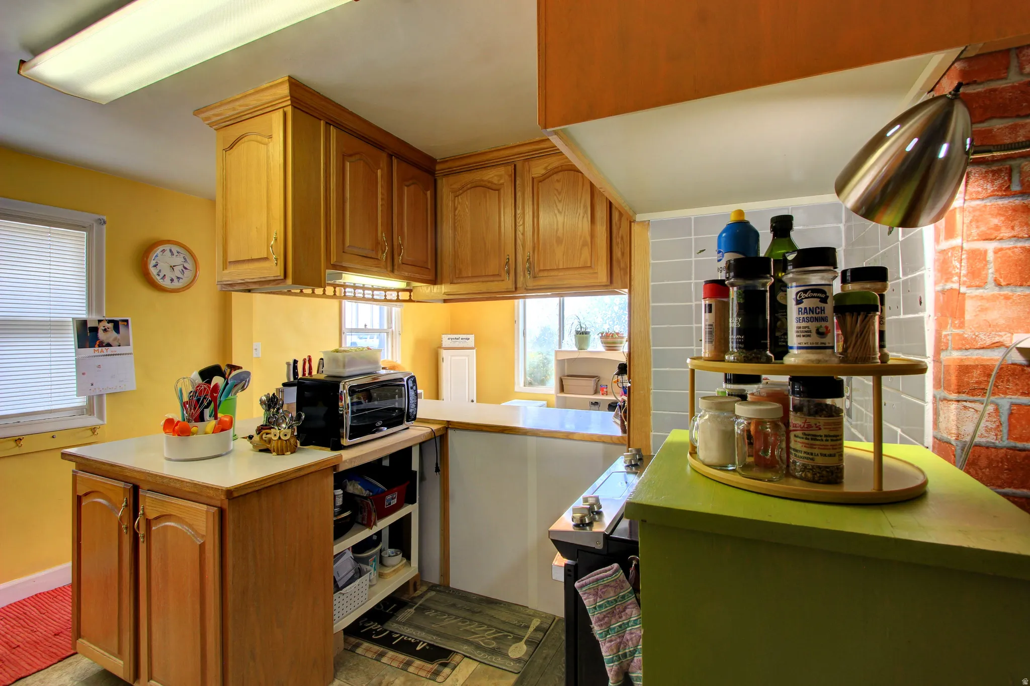 Kitchen featuring light wood cabinetry, white countertops, a tiled backsplash, and an exposed brick wall accent