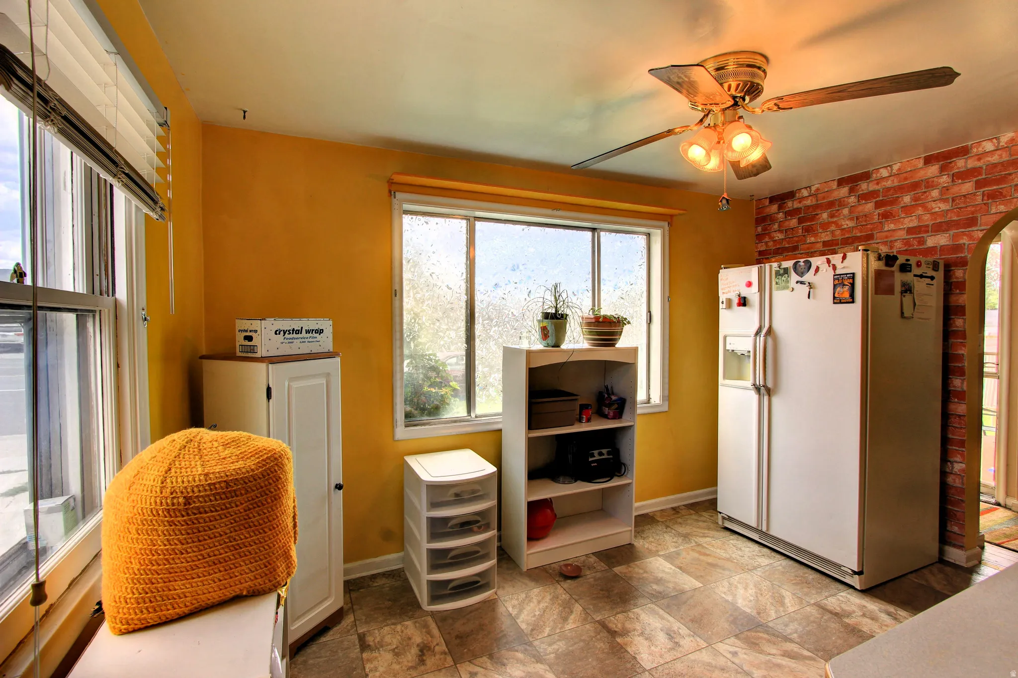 Kitchen area featuring a ceiling fan with light fixture, brick accent wall, and multiple windows