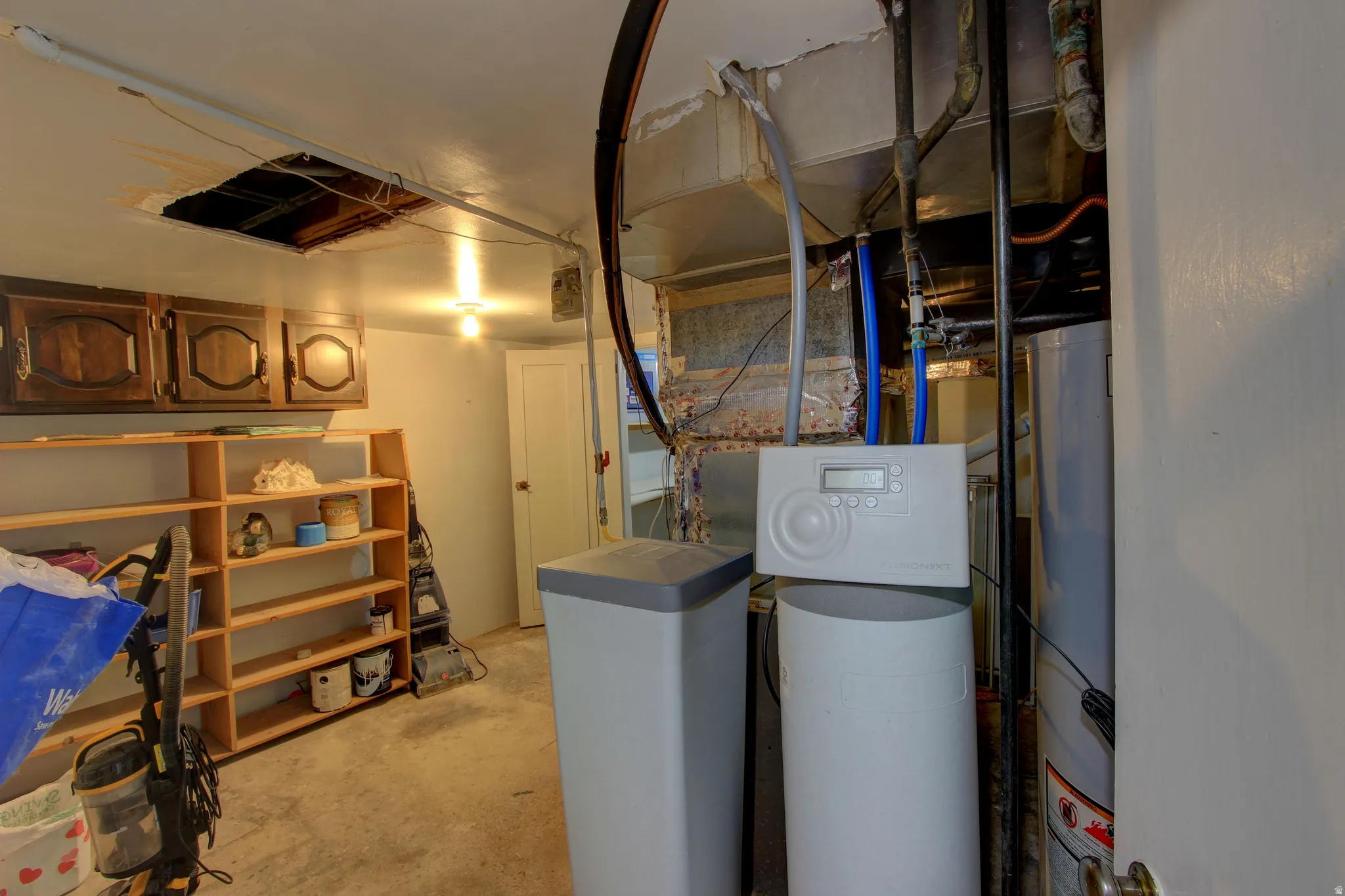 Utility room featuring a water heater, water softener system, exposed ductwork, overhead lighting, and concrete flooring