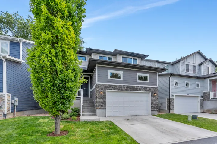 Contemporary multi-level exterior with a stone facade accent, gray siding, and a white garage door