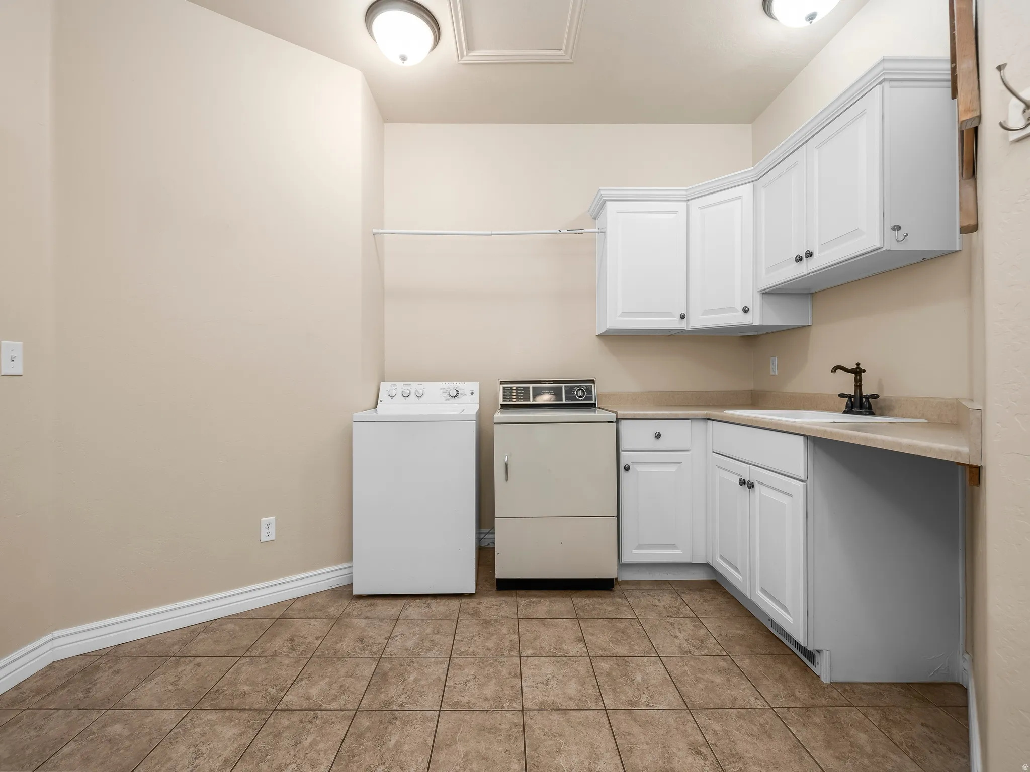 Utility room featuring tile flooring, white cabinetry, a built-in sink, and a clothes rod