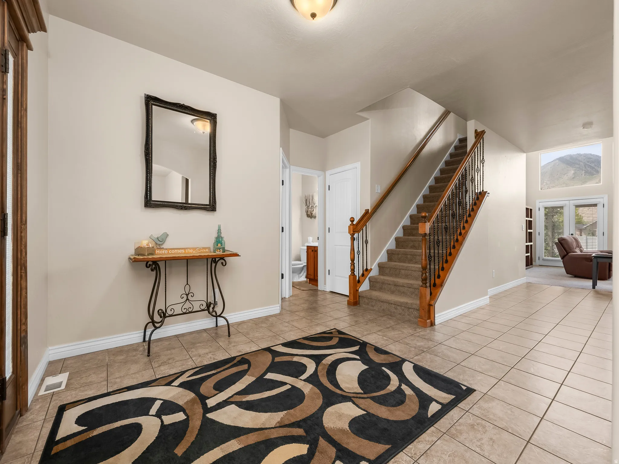 Inviting entry foyer featuring tile flooring, a carpeted staircase with wood handrails and wrought iron balusters, and a mountain backdrop visible through the large windows