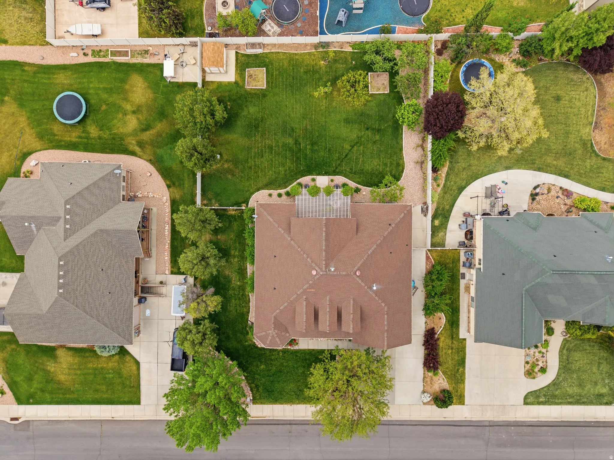 Expansive lot featuring a large green space, mature trees, concrete driveway, and a fenced perimeter