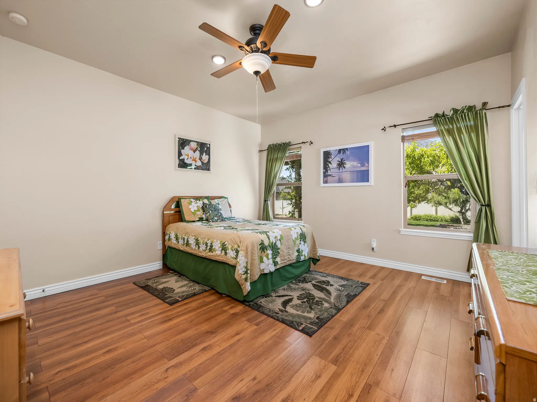 Spacious room featuring wood-finish flooring, two windows with white trim, and a ceiling fan with integrated lighting