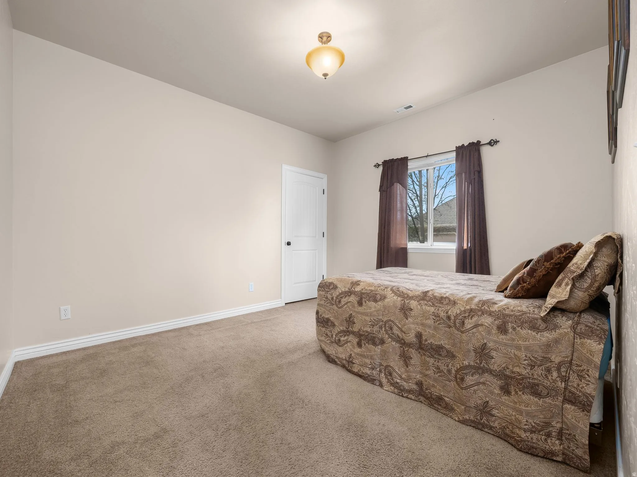 Carpeted room featuring a white paneled door with black hardware, a ceiling-mounted light fixture, and a window with neutral-toned drapes