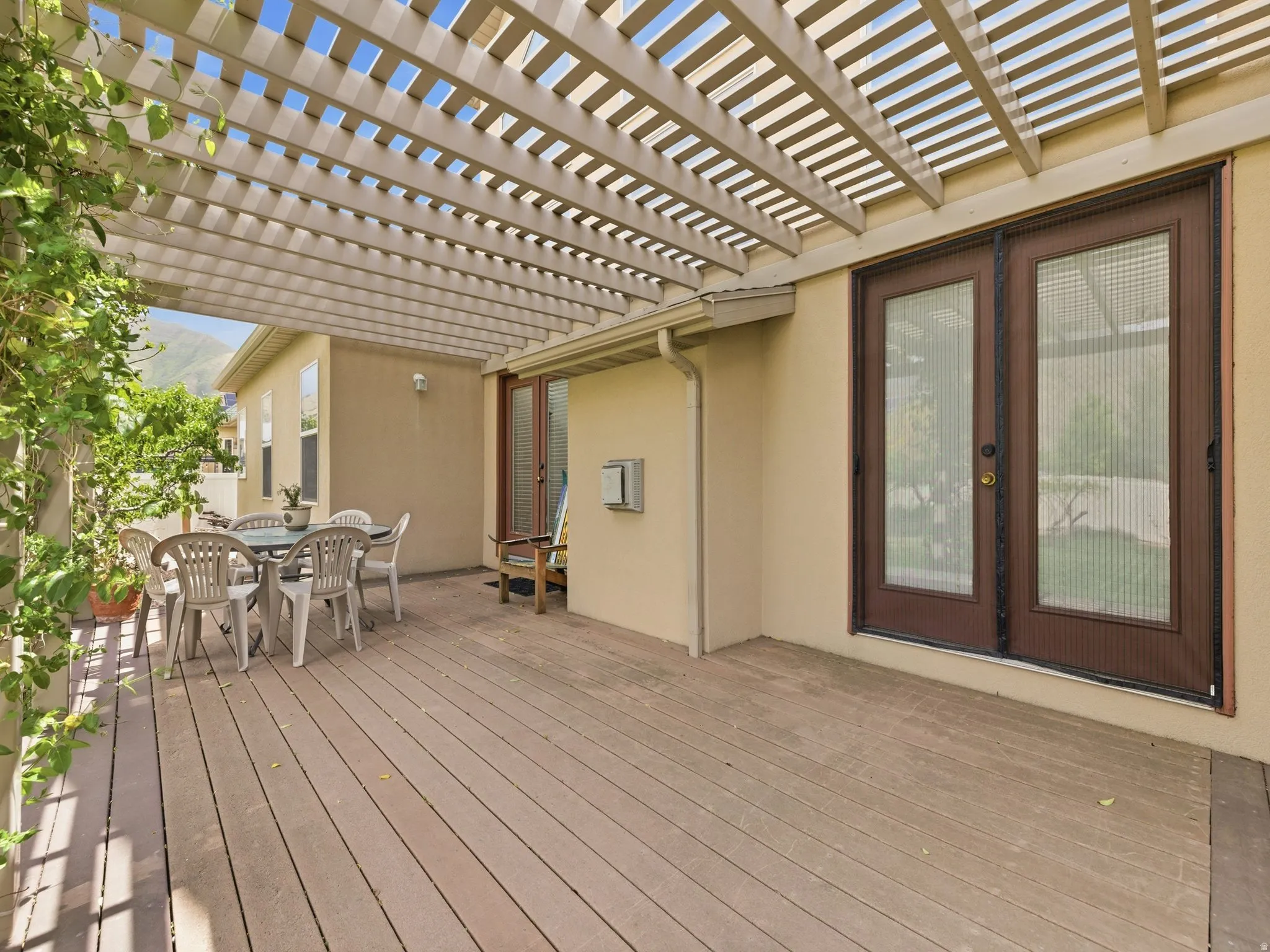 Expansive outdoor deck featuring a light-colored pergola, stucco exterior, and dual French doors with screen inserts