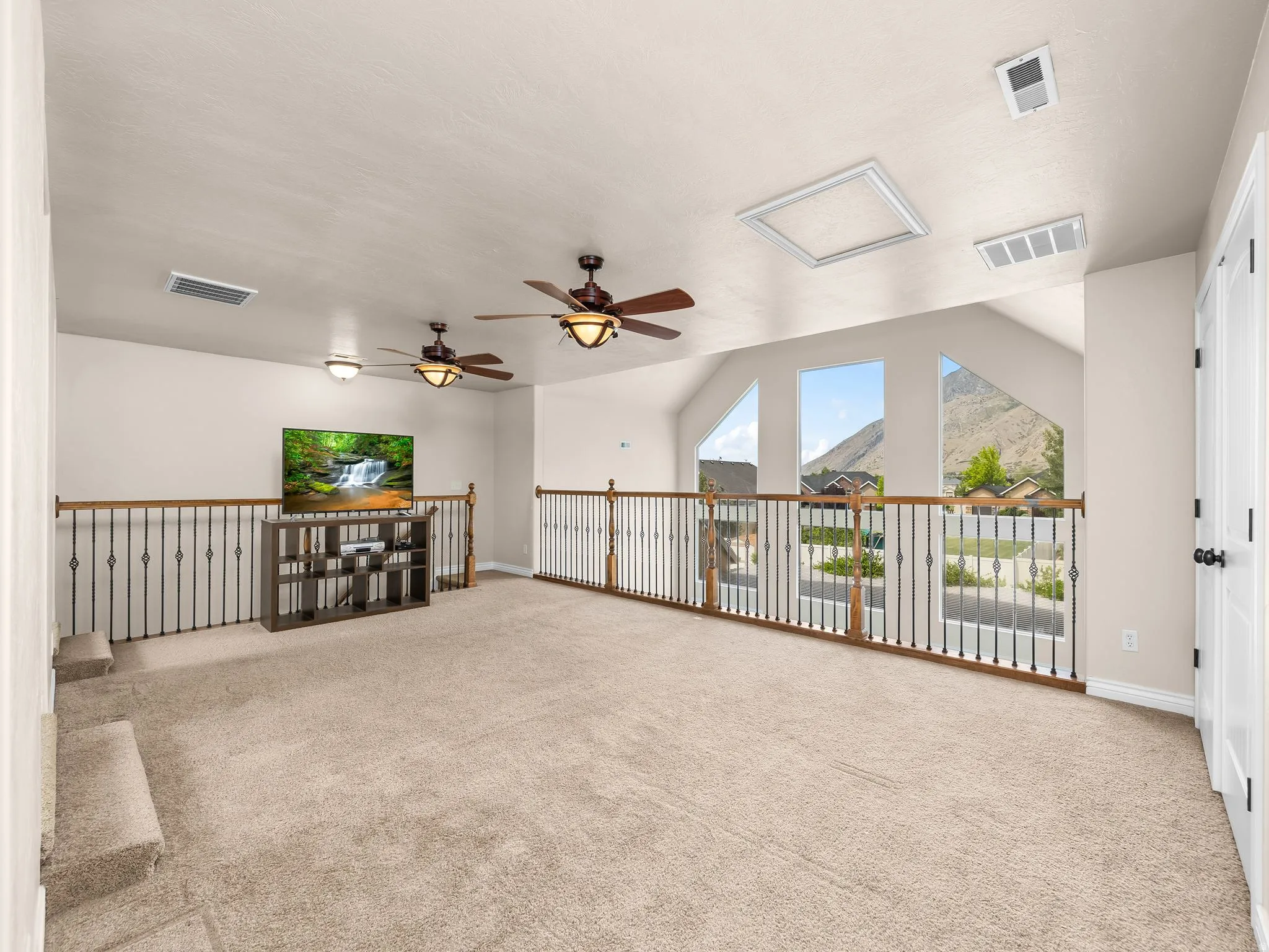 Carpeted loft space featuring an open railing, multiple windows, and two ceiling fans