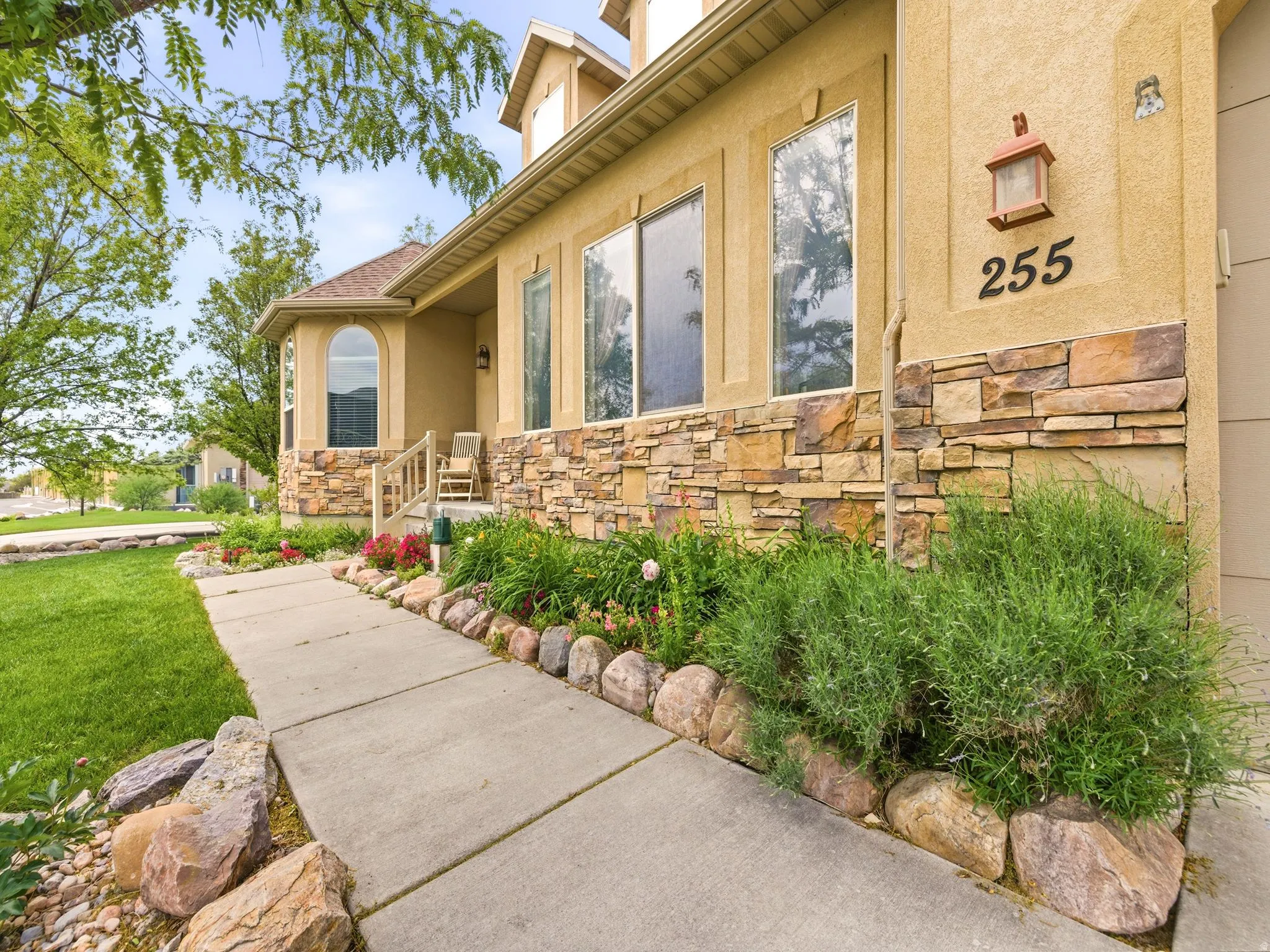 Stucco exterior with stone veneer accents, concrete pathway, established landscaping with natural rock borders, and a covered porch with an arched window