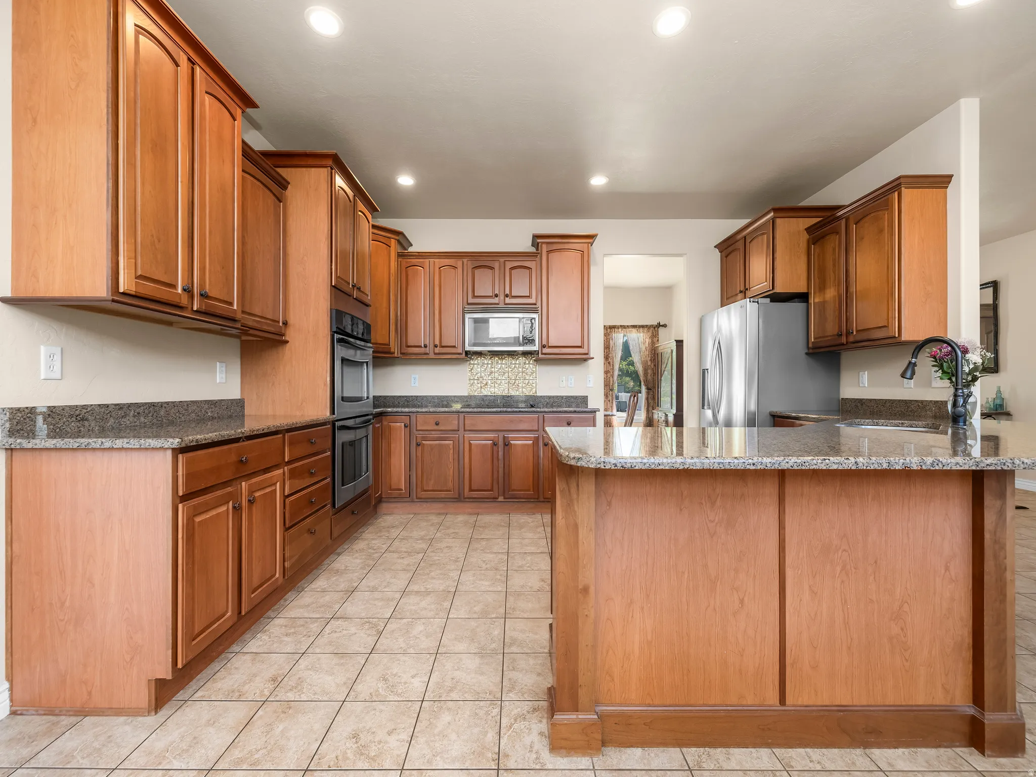Kitchen featuring an eat-at island, recessed lighting, tile flooring, wood cabinetry, and granite countertops