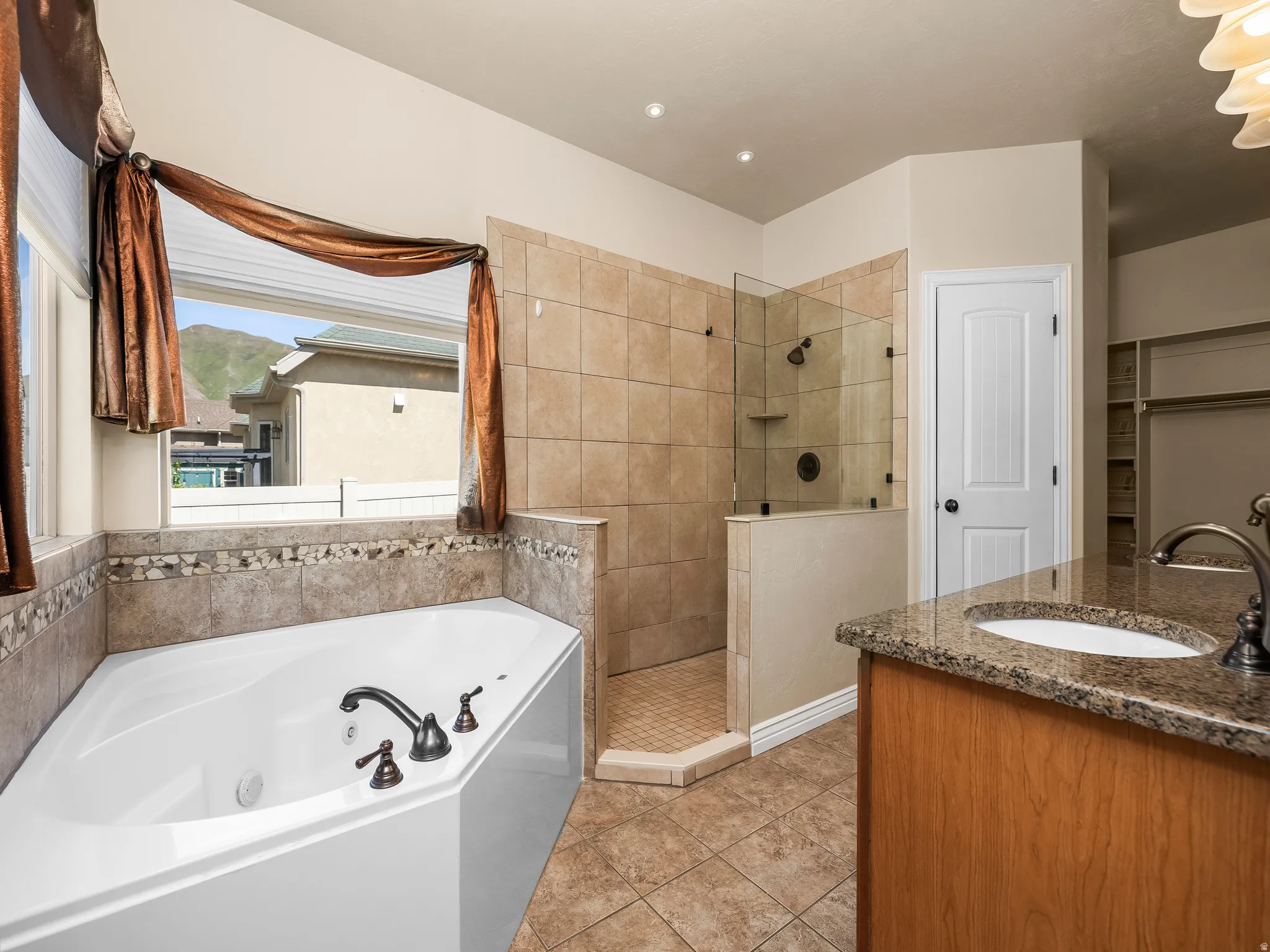 Bathroom featuring a corner soaking tub with bronze fixtures, a tiled walk-in shower with a glass enclosure, and a vanity with a granite countertop and undermount sink