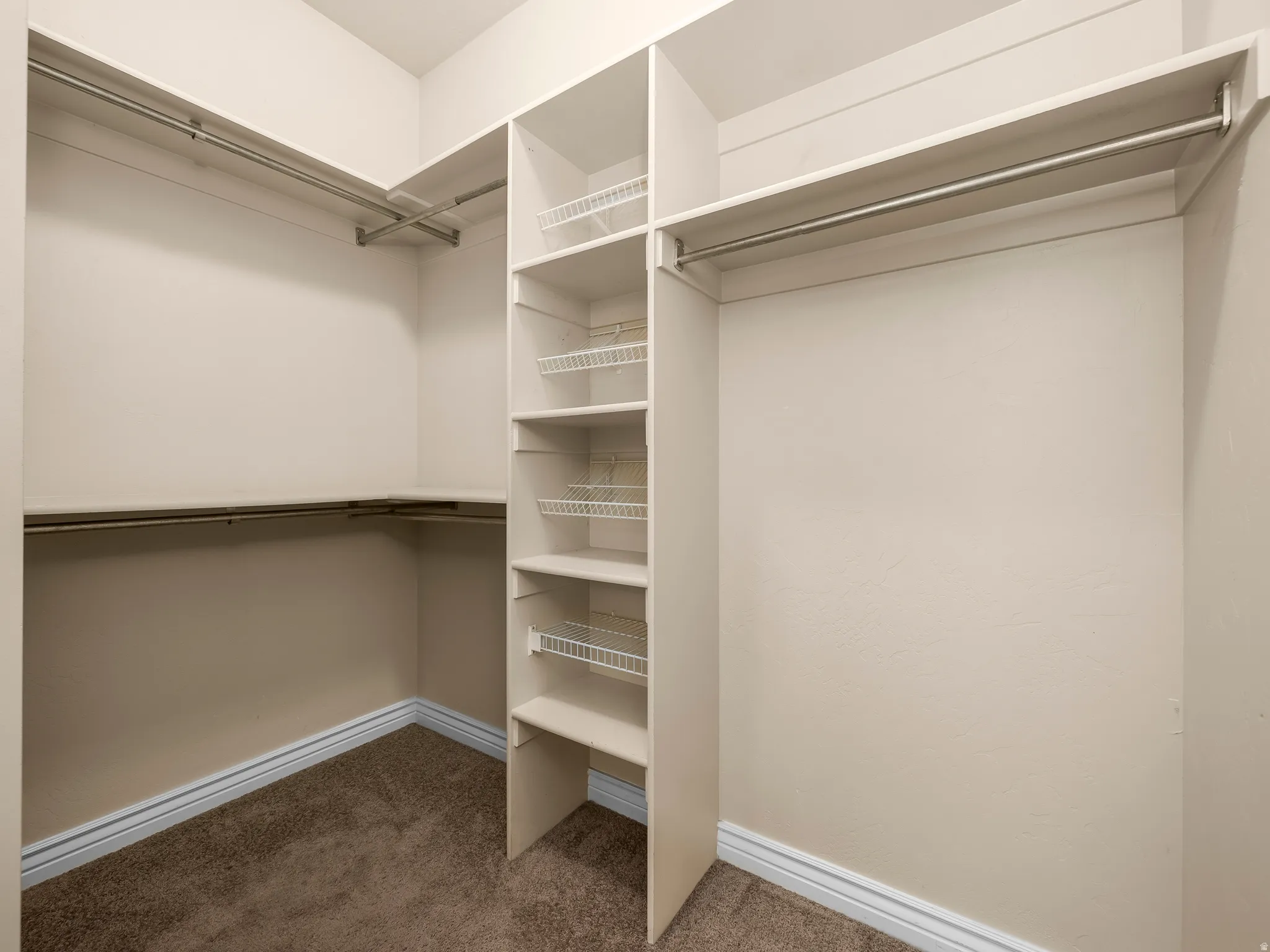 Walk-in closet featuring built-in shelving, multiple hanging rods, wire basket drawers, and a neutral carpet