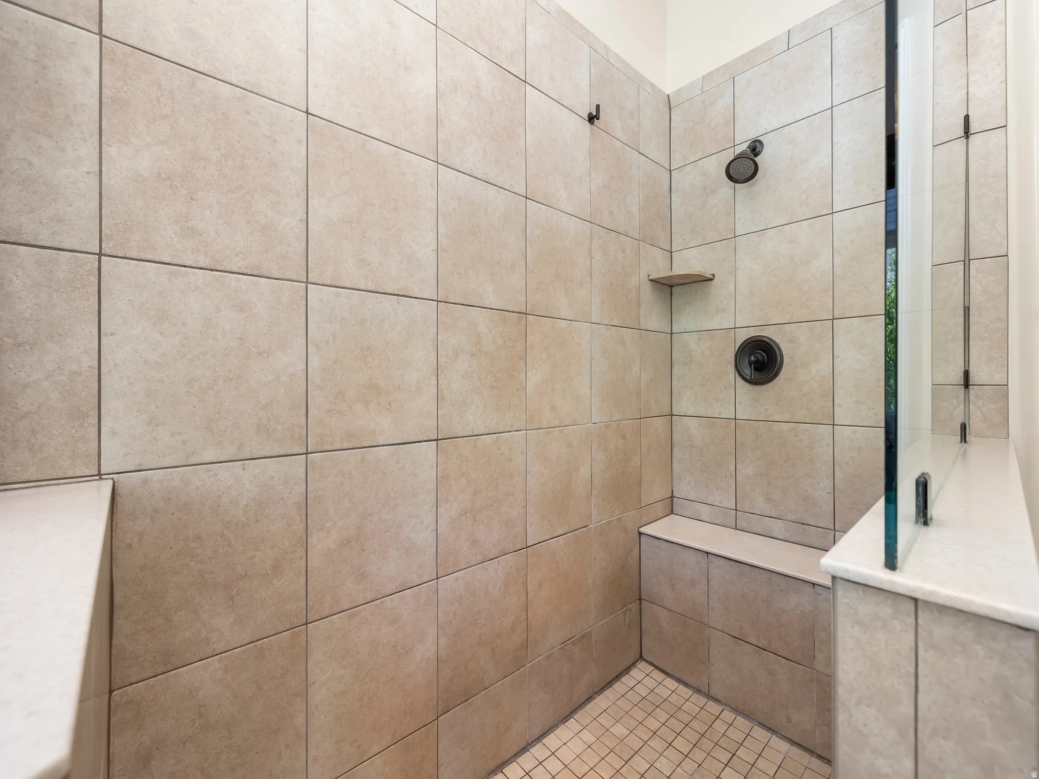 Walk-in shower with full-height tile surround, integrated bench seating, built-in shelving, dark bronze fixtures, and a glass partition