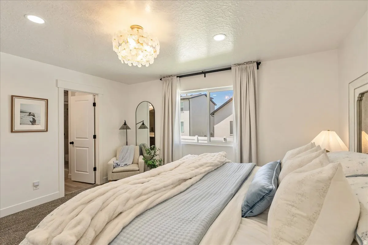 Spacious bedroom featuring recessed lighting, a decorative ceiling fixture, a window with curtains, and a doorway opening to an additional area