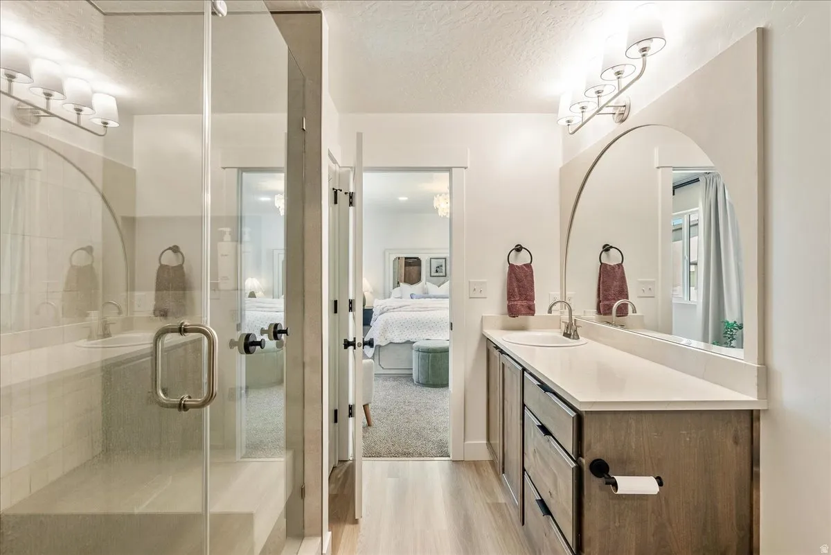 Bathroom featuring a glass-enclosed shower with a built-in bench, a wood-finish vanity with a single sink and light-toned countertop, a large arched mirror, and wood-finish flooring