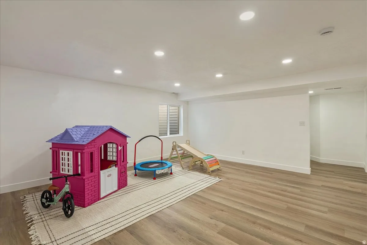 Expansive room featuring wood-finish flooring, recessed lighting, white walls, white baseboards, and a window with horizontal blinds