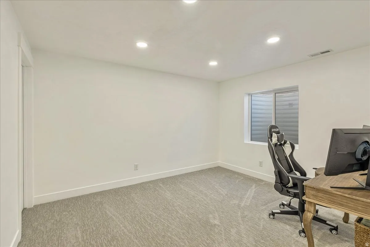 Bright room featuring light-toned carpeting, crisp white walls, recessed ceiling lighting, a white-framed window, and a white baseboard trim